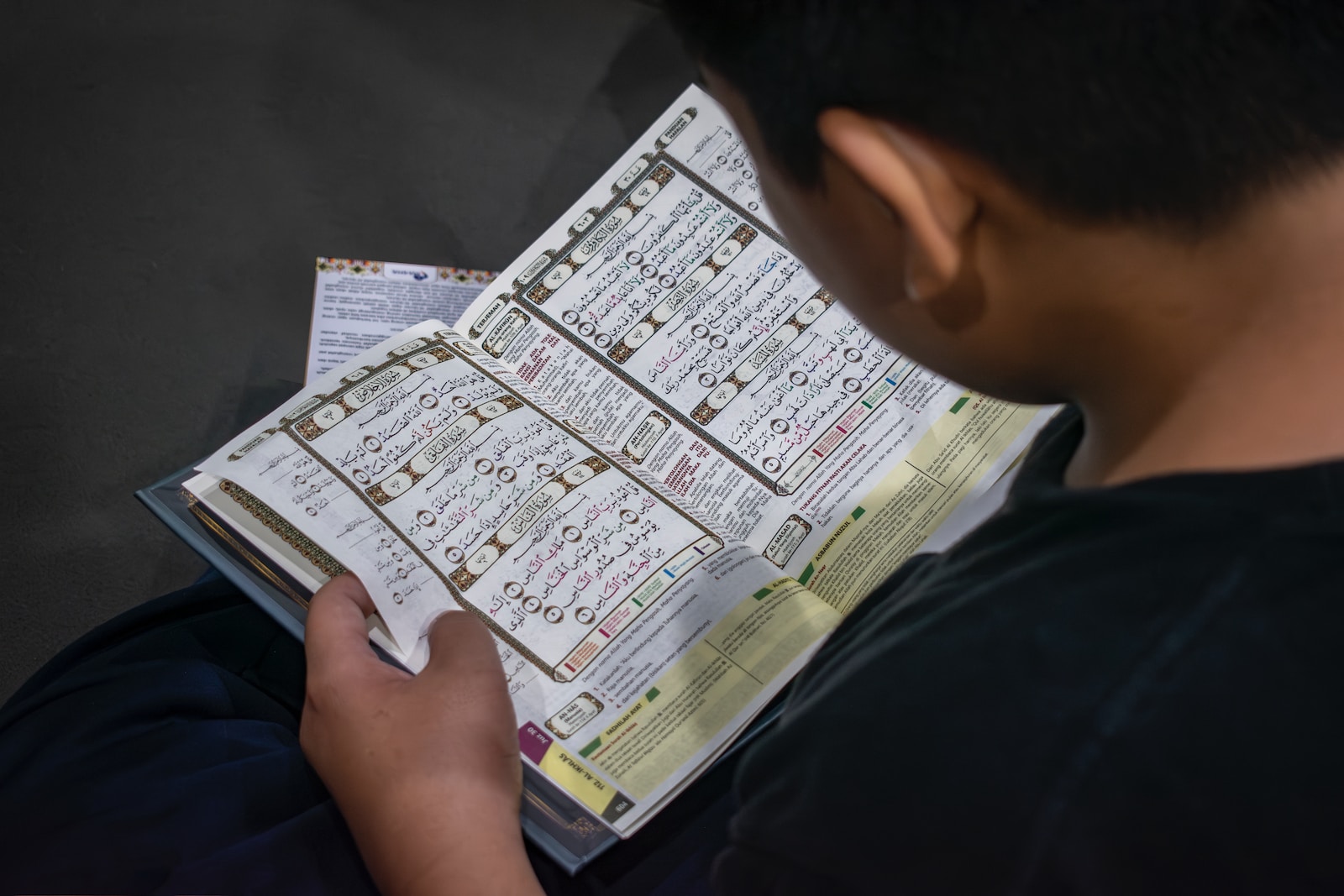 a young boy is reading the quraan memorising a book with numbers on it